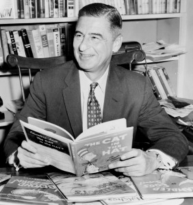 Dr Seuss seated at desk covered with his books, World Telegram and Sun photo by Al Ravenna